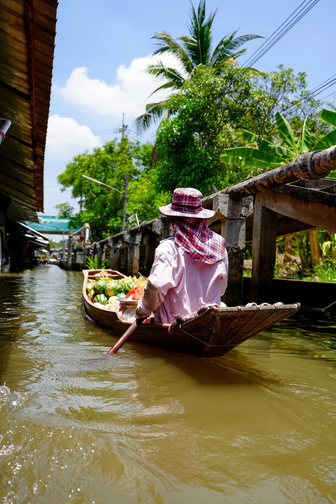 A vendor paddling a fruit-laden boat through a Bangkok floating market
