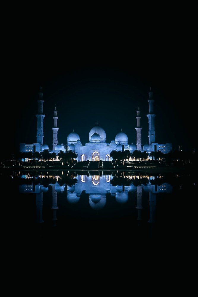 Sheikh Zayed Grand Mosque lit blue at night, reflected in the water in front of it