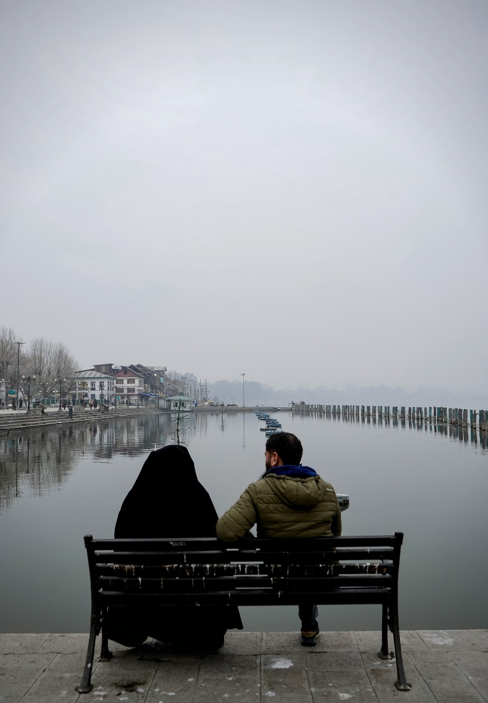 A couple sitting on a bench looking out over misty Dal Lake in Kashmir, photographed by Ashiq