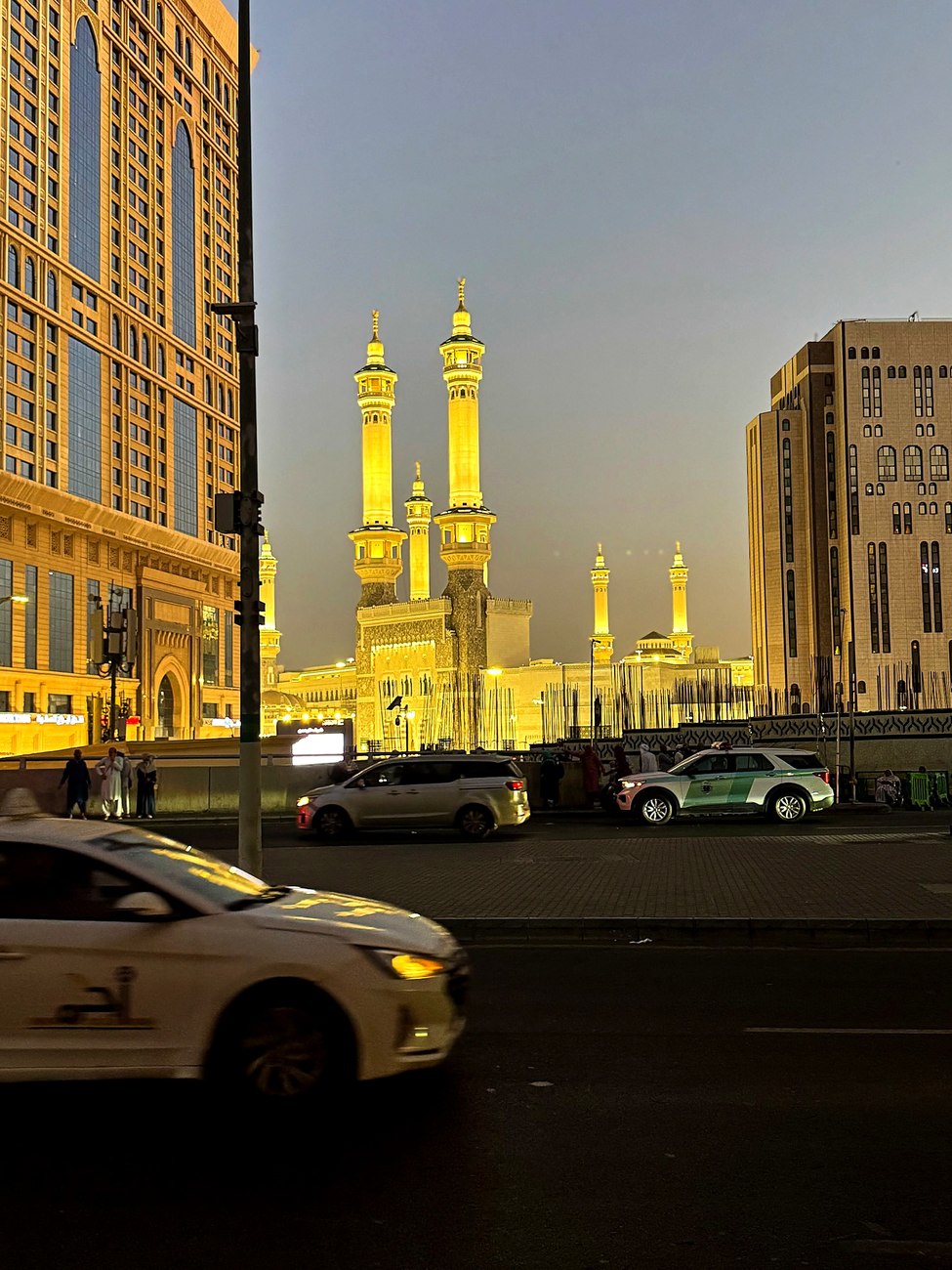 The illuminated minarets of the Masjid al-Haram seen from a street in Makkah at dusk